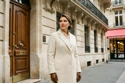 Femme élégante en manteau ivoire devant un immeuble haussmannien parisien, ambiance luxe et raffinement éditorial
